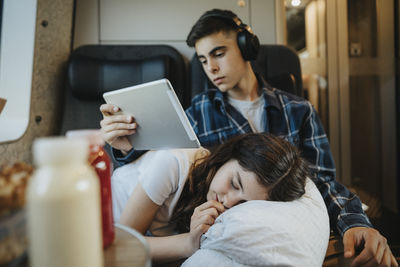 Boy holding tablet pc with sister taking nap in train