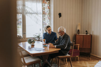 Female care assistant talking to senior man while taking medicine at home