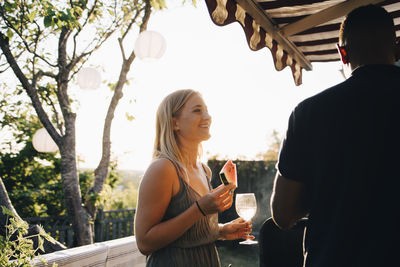 Woman eating watermelon and having wine while talking to friend in party