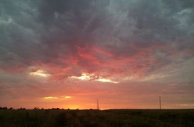 Scenic view of landscape against cloudy sky at sunset