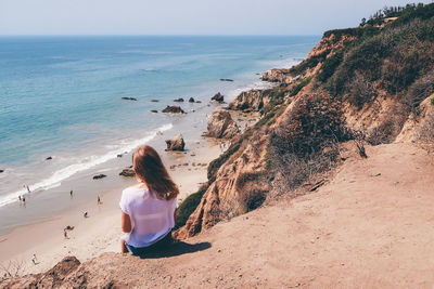 Rear view of woman sitting on mountain at beach