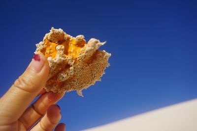 Close-up of hand holding ice cream against blue sky