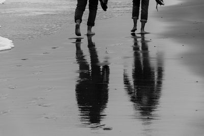 Low section of people walking on wet beach