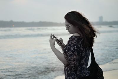 Beautiful woman standing at beach against sky