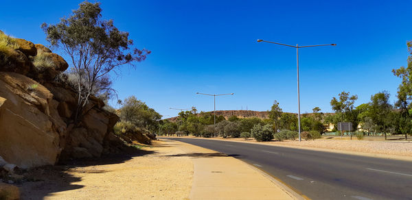 Street amidst trees against blue sky