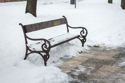 Empty bench in snow covered park during winter
