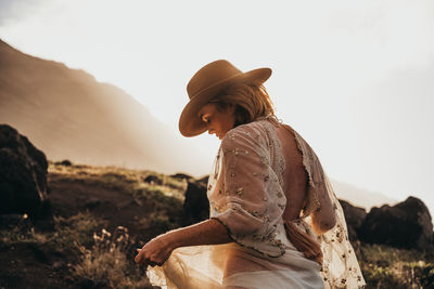 Side view of woman sitting on land against sky