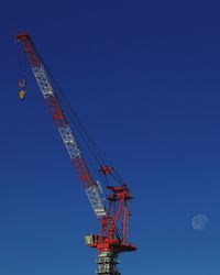 Low angle view of crane against clear blue sky