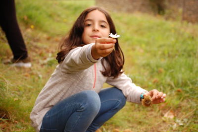 Cute girl holding flower while crouching on field