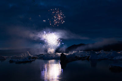 Firework display over lake against sky at night