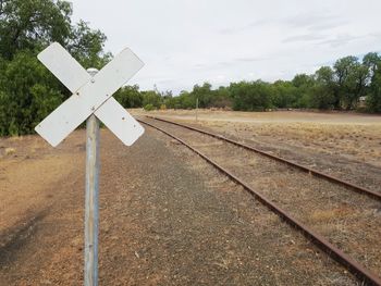 Information sign on railroad track by field against sky