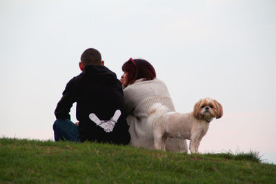 Rear view of woman with dog sitting against clear sky