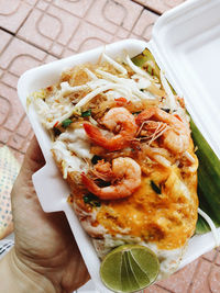 Cropped hand holding pad thai in disposable container