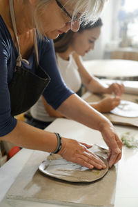 Woman rolling clay, making ceramic plate in studio with floral pattern. handmade creative work