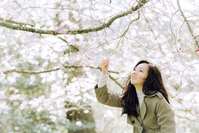 Portrait of young woman standing against cherry blossom