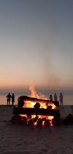 Silhouette people on beach around bonfire against sky at dusk