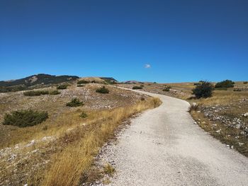 Road amidst land against clear blue sky