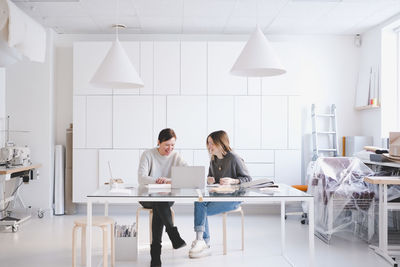 Smiling female fashion designers discussing over laptop at desk in studio