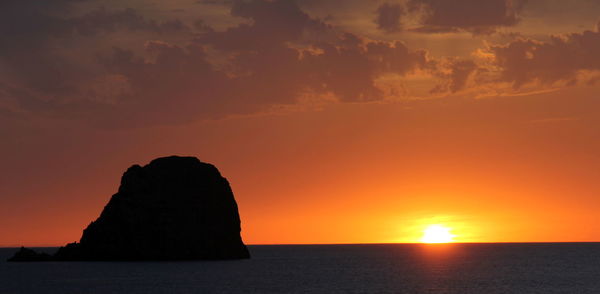 Silhouette rock in sea against sky during sunset