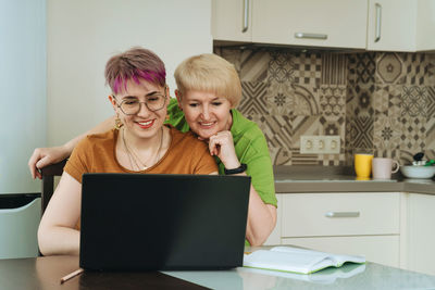 Adult mother and daughter, hugging and smiling, look at the laptop screen