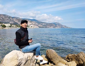 Man sitting on rock by sea against sky