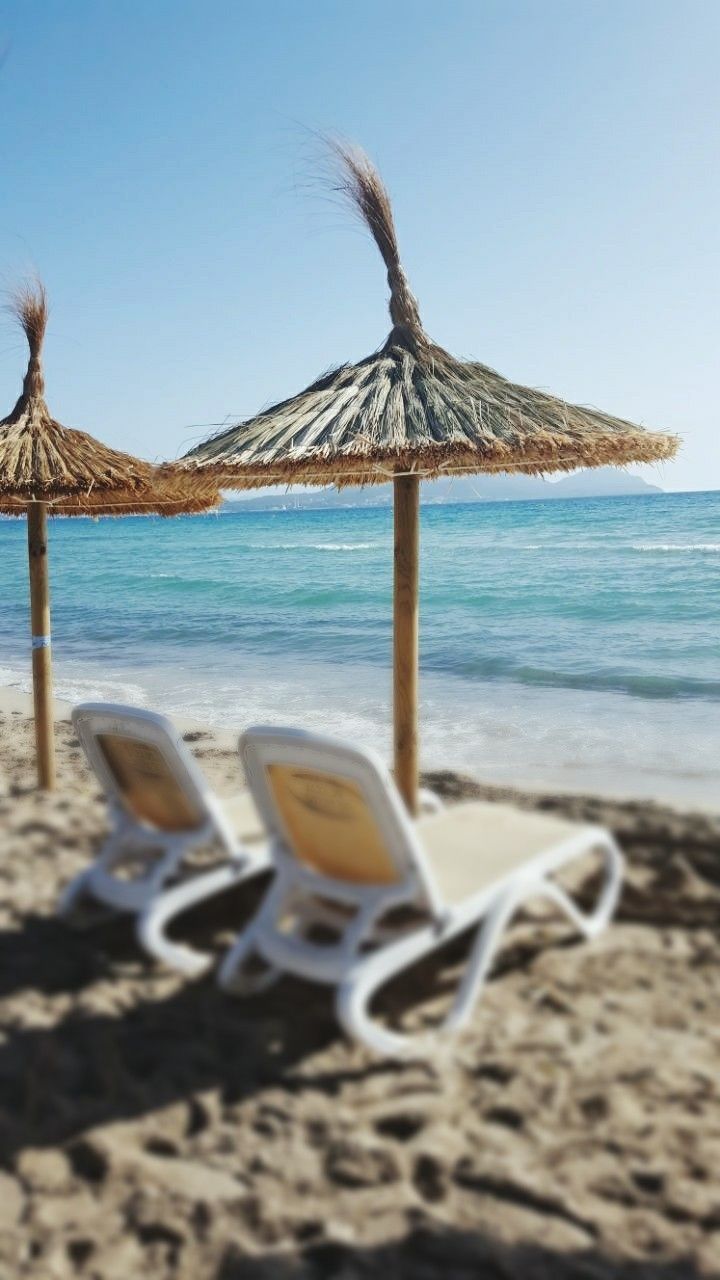 CLOSE-UP OF LOUNGE CHAIRS ON BEACH AGAINST CLEAR SKY