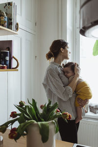 Mother looking through window while carrying male toddler at home