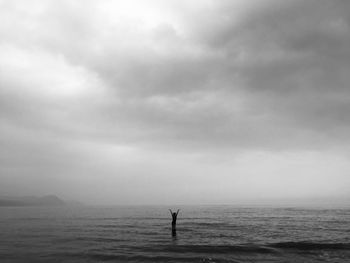 Person standing in sea against cloudy sky