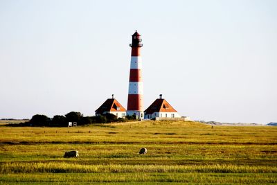 Lighthouse on field by building against clear sky