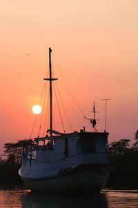 Sailboats moored in sea against sky during sunset