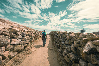 Rear view of man on footpath amidst stone walls against sky