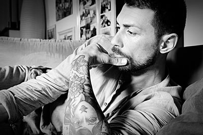 Thoughtful man tattooed hand resting on sofa at home