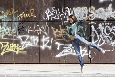 Full length of woman dancing against graffiti on wall