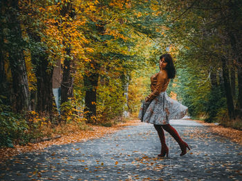 Full length of woman spinning on road amidst trees during autumn