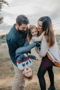 Delighted couple playing with little children while having fun together in countryside at weekend