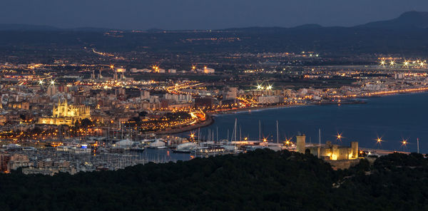 High angle view of illuminated city by sea against sky