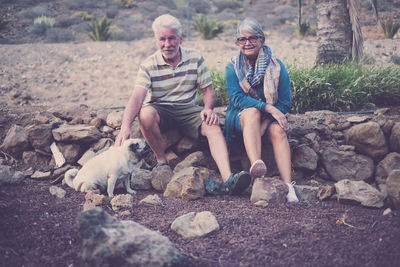 Senior couple sitting on rocks with dog on ground