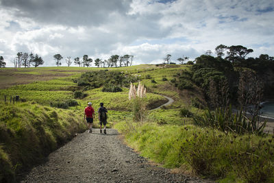 Rear view of men walking on dirt road against sky