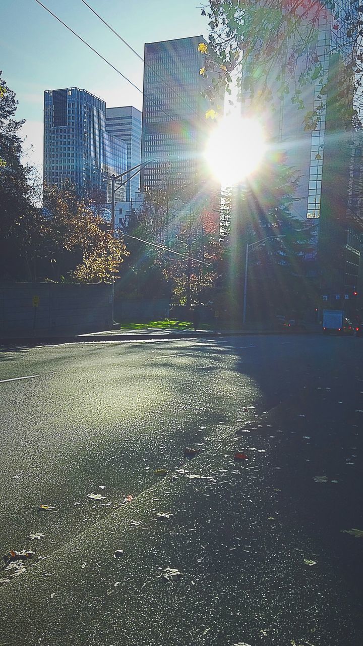 building exterior, architecture, built structure, city, street, sunlight, sunbeam, sun, transportation, lens flare, car, road, building, wet, city street, land vehicle, tree, season, day, outdoors