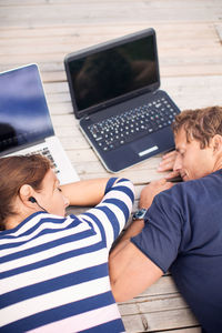 High angle view of mature couple sleeping with laptops on pier