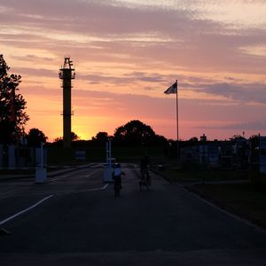 Silhouette people on street against sky at sunset