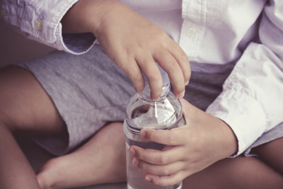 Midsection of child opening water bottle while sitting at home