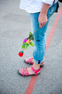 Low section of woman holding flower while standing on road