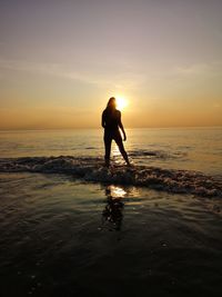 Silhouette woman standing on beach against sky during sunset