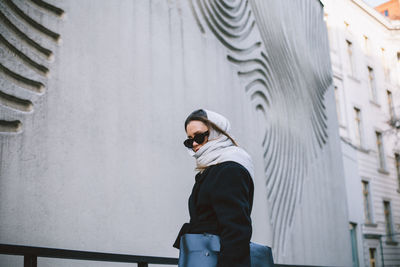 Low angle view of woman wearing sunglasses standing against wall