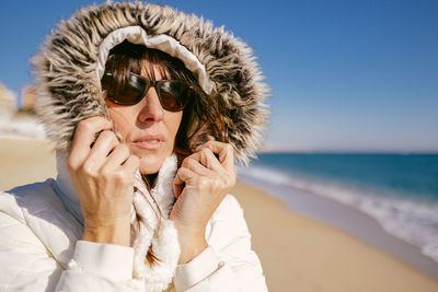 Beatiful mature woman in white jacket and sunglasses on a sunny winter day at the beach