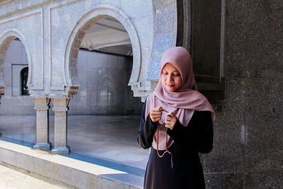 Woman in hijab holding counting rosary beads while praying at mosque