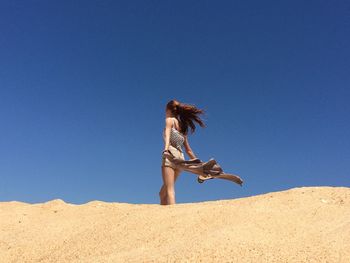 Low angle view of woman holding jacket against clear blue sky at desert