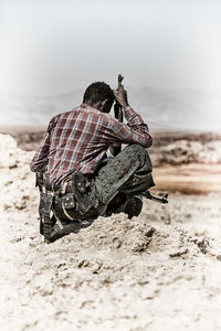 Rear view of man photographing on sand at beach against sky