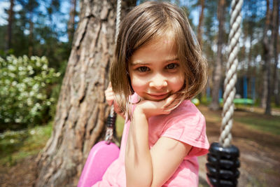 Portrait of smiling girl sitting on swing in park